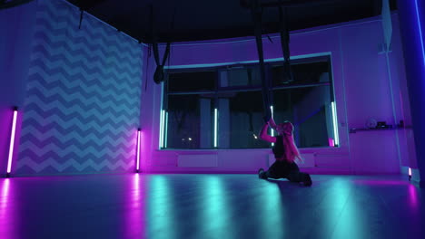 A-woman-does-yoga-and-stretching-on-a-hanging-hammock-in-neon-light.-Young-pretty-slim-body-fitness-girl-practicing-fly-yoga-in-the-gym.